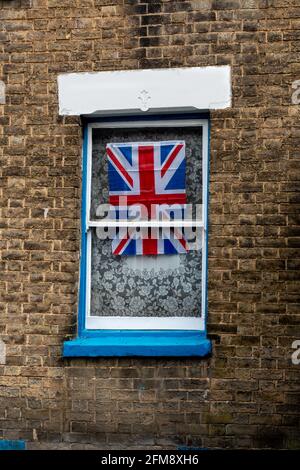 Union flag displayed in a sash window with a net curtain set in a brick wall. Cambridge, UK Stock Photo