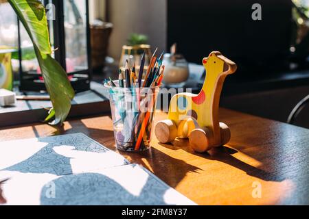 Wooden toy giraffe, colored pencils and a coloring book on a wooden table. Stock Photo