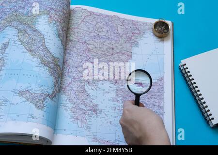 West side of Turkey on a map in  a book, .A woman handling a  magnifying glass, showing the the city  Istanbul and a compass left side of the page. Stock Photo