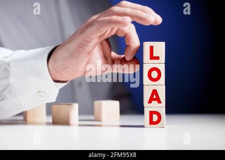 The word load written on tiered wooden cubes with a businessman hand is about to flip the cubes. Overwork, overload and offloading in business or work Stock Photo