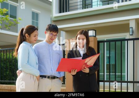 Asian woman Real estate broker agent showing a house detail in her file to the young Asian couple lover looking and interest to buy it. Buying a new h Stock Photo