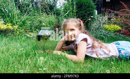 The girl lies on the lawn. The concept of life with children in the country. A schoolgirl is carrying out a school project to create a homemade aquati Stock Photo