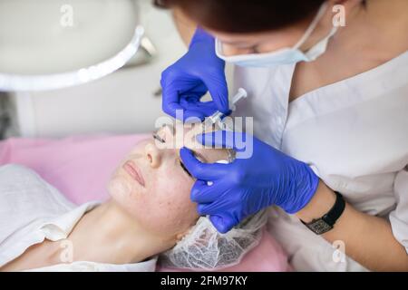 Cosmetology skin care. Doctor cosmetologist makes rejuvenating facial injections for tightening and smoothing wrinkles on the forehead of beautiful, young woman Stock Photo