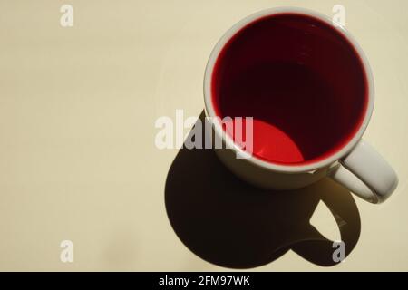 Beige cup with red inside on a beige table. Light and shadow. Top view. Stock Photo