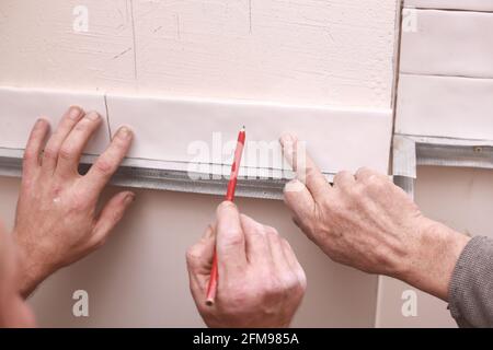 Stylish trendy white ceramic tiles on the kitchen wall. Hands in the process of laying white rectangular tiles on the bathroom wall. Renovation of apa Stock Photo