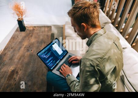 Young man mobile developer with laptop, writes program code on a computer, programmer work in modern office. Stock Photo