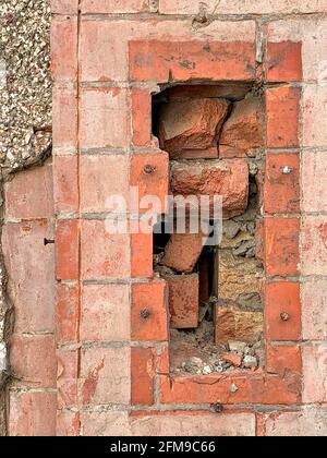 Damaged red brick boundary wall revealing brick rubble Stock Photo