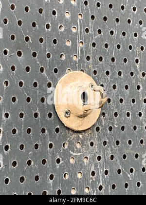 Painted metal hook fixed to perforated security screen on building Stock Photo