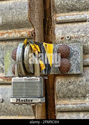Padlock on metal street doors, with black and yellow hazard tape Stock Photo