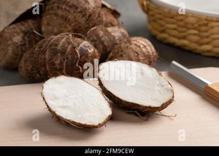 Fresh whole and halved taro vegetable on a cutting board Stock Photo