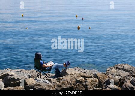 Istanbul, Turkey - April 21, 2021 : A modern young woman is reading her book on rocks and enjoying the sun at Suadiye coastline. Stock Photo