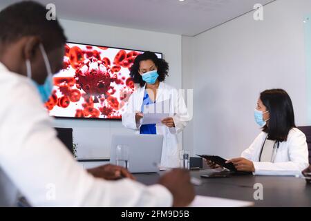 African american female doctor wearing face mask giving presentation to team of doctors Stock Photo