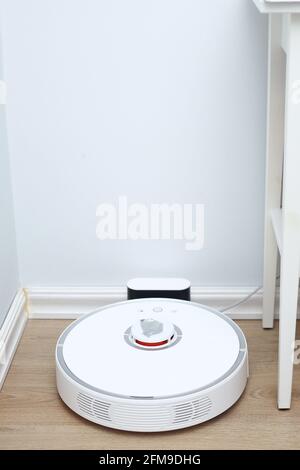 Robotic vacuum cleaner on laminate wood floor charging from base station. Smart cleaning technology. robot vacuum cleaner return to charging at dock i Stock Photo