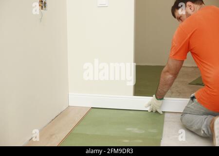 the worker installs plinths in the apartment. Installing a white plastic skirting board on a laminate - adjusting and trimming. Stock Photo