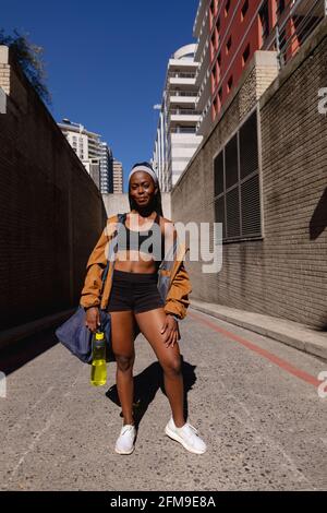 Smiling fit african american woman with gym bag standing in street in city Stock Photo