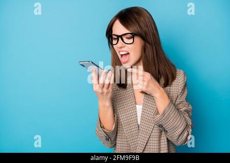 Photo portrait of angry woman pointing finger screaming at phone holding in one hand isolated on vivid blue colored background Stock Photo