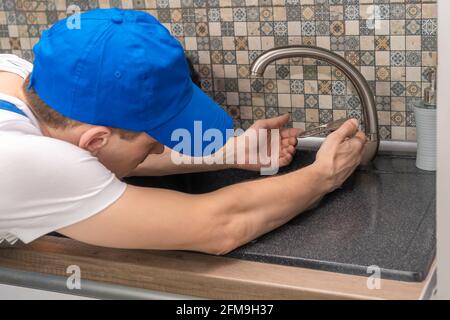 Male plumber in uniform checks the faucet in the kitchen close-up. Repair services Stock Photo