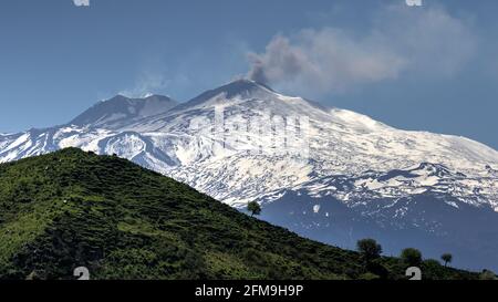 Italy, Sicily, spring, Etna, snow-covered, cloud of smoke, green hill in the foreground, sky light blue Stock Photo