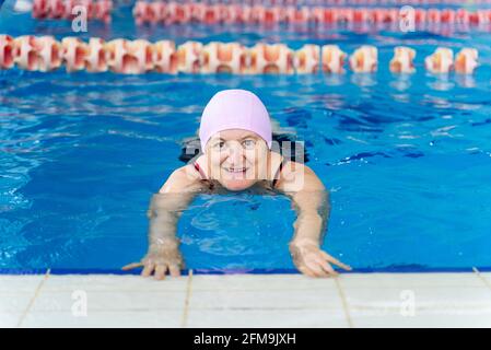Happy middle aged woman learning to swim in a swimming pool. Stock Photo