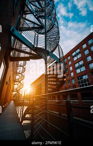 Winding stairs in the old Warehouse District. Narrow canal and red brick buildings of Speicherstadt in Hamburg in the warm sunset light. low angle shot. Stock Photo