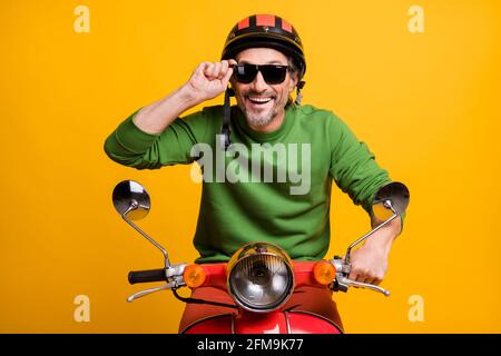 Photo of funky positive guy ride scooter wear helmet eyewear green sweater isolated yellow color background Stock Photo