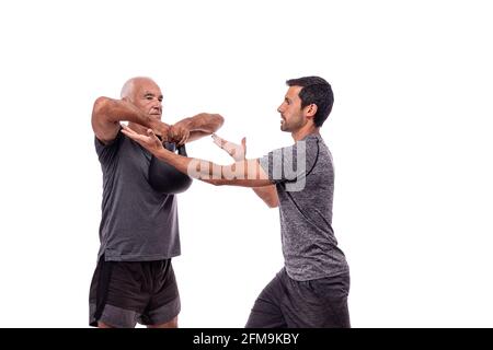 Elderly male client exercising with a fitness trainer, raises dumbbell. On a white isolated background. Stock Photo