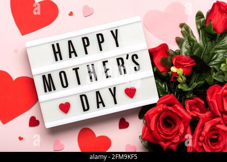 Happy Mother's Day.Lightbox with the word Happy Mother's Day next to hearts and bouquet of red red roses on a pink background Stock Photo