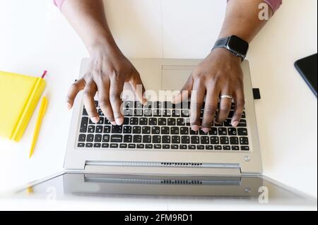 A male hands on the laptop keyboard. Top view an African-American guy is typing email, programmer is develops software, cropped photo, a face is not visible, close-up picture Stock Photo