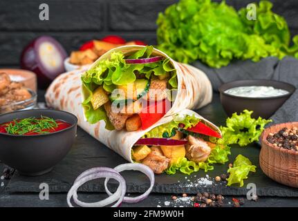 Traditional oriental shawarma close-up on a black background. Meat, French fries, vegetables and salad wrapped in pita bread. Quick snack, fast food. Stock Photo