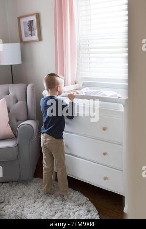 A big brother stands and watches his new little sister on her changing table Stock Photo