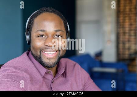 Call center operator wearing headset looks at the camera with cheerful smile, headshot of cheerful African-American man in headset, technical support worker in headphones in touch Stock Photo