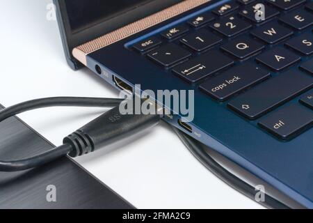 External hard drive disc connected to laptop via usb 3.0 cable. Concept of data storage on portable hdd. Close-up on white surface with shadow. Stock Photo