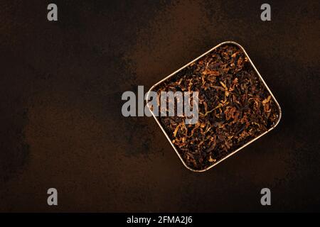 Close up tin full of ready rubbed long coarse cut pipe tobacco blend over grunge brown background, elevated top view, directly above Stock Photo