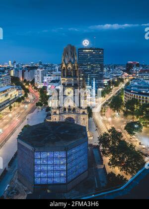 Illuminated Memorial Church on Breitscheidplatz in Berlin with a view of the Europa Center in the evening. Stock Photo