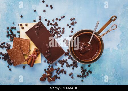 Melted chocolate in copper pan and  bars of dark and white chocolate beside on rustic blue surface. Top view, blank space Stock Photo