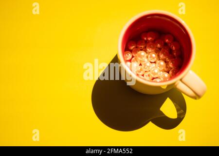 Cup with beige pearl beads inside on a yellow table. Light and shadow. Top view. Stock Photo