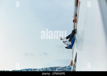 The couple are sailing on a pleasure ferry with their legs dangling from the deck of the second floor. Istanbul, Turkey - 28.07.2017 Stock Photo