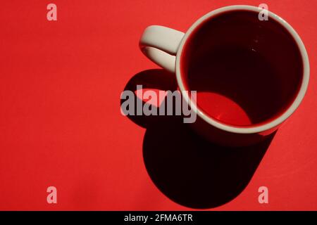 Beige cup with red inside on a red table. Light and shadow. Top view. Copy space Stock Photo