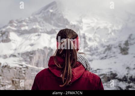 Looking over the shoulders of a young woman in a red jacket towards the snowy mountains Stock Photo