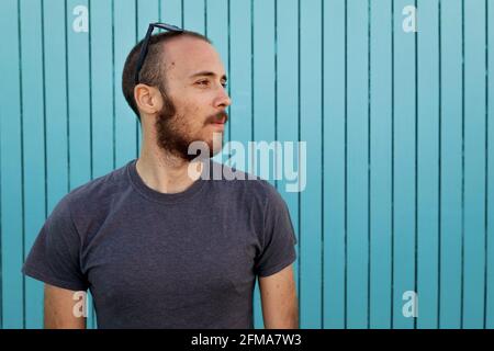 Bearded young man wearing sunglasses over the head is confidently looking away at the Isla Canela beach with a blue wooden wall background Stock Photo