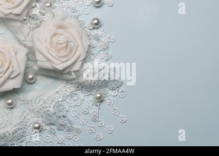 white pearls and lace on a pale blue background with white artificial roses for the concept of  romance or wedding Stock Photo