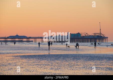 Early morning stroll on the beach, and walking dogs at low tide. The silhouetted shapes of the piers in the background. Brighton & Hove, Sussex, England, UK Stock Photo