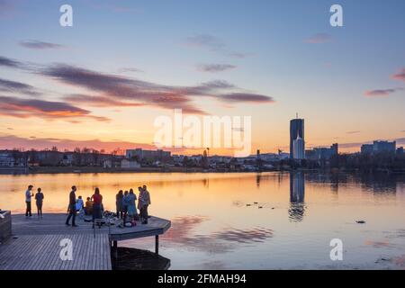 Vienna, young people on a platform at a party above oxbow lake Alte Donau (Old Danube) at fiery sunset, buildings of Donaucity, DC Tower 1, Corona lockdown in 22. Donaustadt, Wien / Vienna, Austria Stock Photo