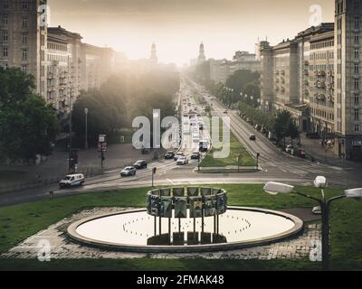 Sunrise behind the fountain of Berlin's Strausberger Platz with the towers of the Frankfurter Tor in the background. Stock Photo