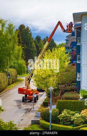 Two workers using a man-lift to access the roof of an apartment building in Steveston British Columbia Canada Stock Photo