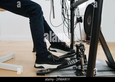 Legs of a little boy playing electronic drums, pedalling. He is wearing jeans and new stylish sneakers. Side view. Stock Photo