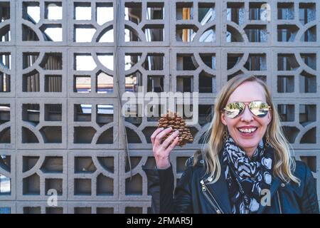 Attractive blonde haired woman holds up large pinecone against geometric lattice Stock Photo