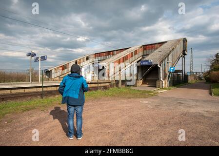 Germany, Saxony-Anhalt, Schönebeck, a man stands at an abandoned train station in front of a rusted and covered pedestrian crossing. Stock Photo