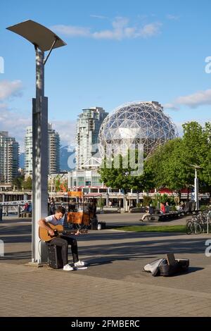 Young man playing the guitar on walkway at the Olympic Village on False Creek, Vancouver, BC, Canada Stock Photo