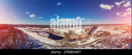 View from above of the countryside and brook on a winter sunny day. Snowy nature landscape with blue sky. Panorama from 21 images Stock Photo